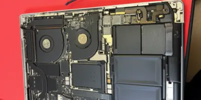 A disassembled MacBook Pro showing the internal motherboard, cooling fans, and battery during a repair process in Auckland.