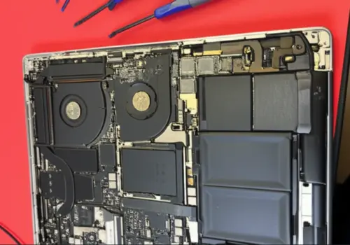 A disassembled MacBook Pro showing the internal motherboard, cooling fans, and battery during a repair process in Auckland.
