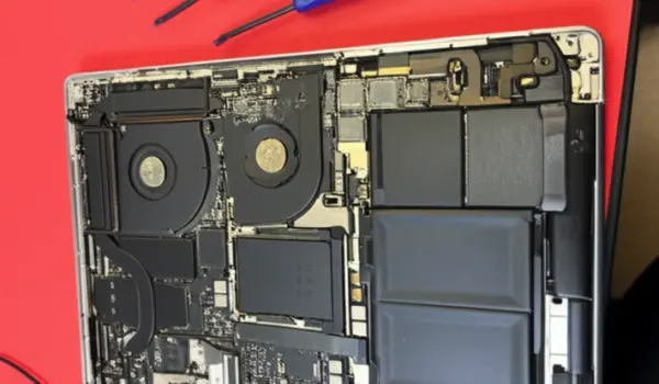 A disassembled MacBook Pro showing the internal motherboard, cooling fans, and battery during a repair process in Auckland.