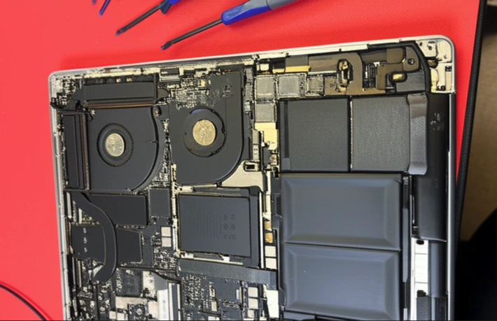 A disassembled MacBook Pro showing the internal motherboard, cooling fans, and battery during a repair process in Auckland.