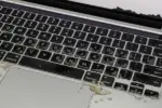 A MacBook Pro A2442 with visible liquid damage on the keyboard, showing coffee spills and corrosion during repair diagnostics.