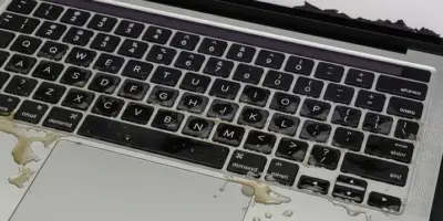 A MacBook Pro A2442 with visible liquid damage on the keyboard, showing coffee spills and corrosion during repair diagnostics.
