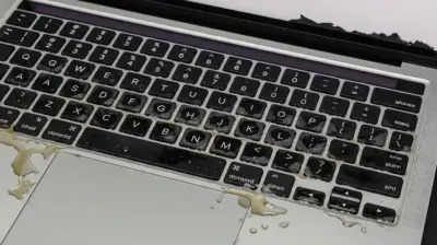 A MacBook Pro A2442 with visible liquid damage on the keyboard, showing coffee spills and corrosion during repair diagnostics.