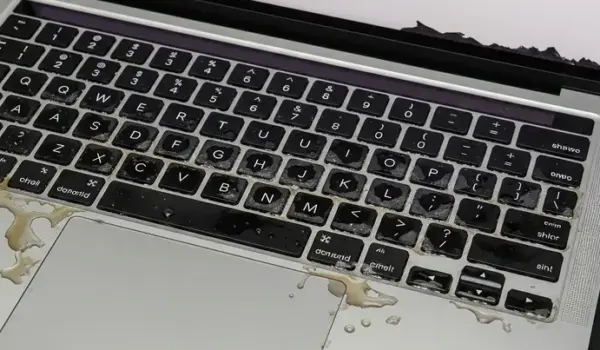 A MacBook Pro A2442 with visible liquid damage on the keyboard, showing coffee spills and corrosion during repair diagnostics.