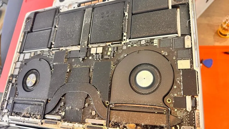 Dead MacBook Pro A2485 Motherboard Recovery Case Sudy 1 Dust-covered MacBook Pro motherboard with visible cooling fans and battery before undergoing complex repair in Auckland.