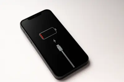 An iPhone lying on a flat surface showing a nearly empty battery icon with a charging cable symbol, illustrating the need to replace an iPhone battery.