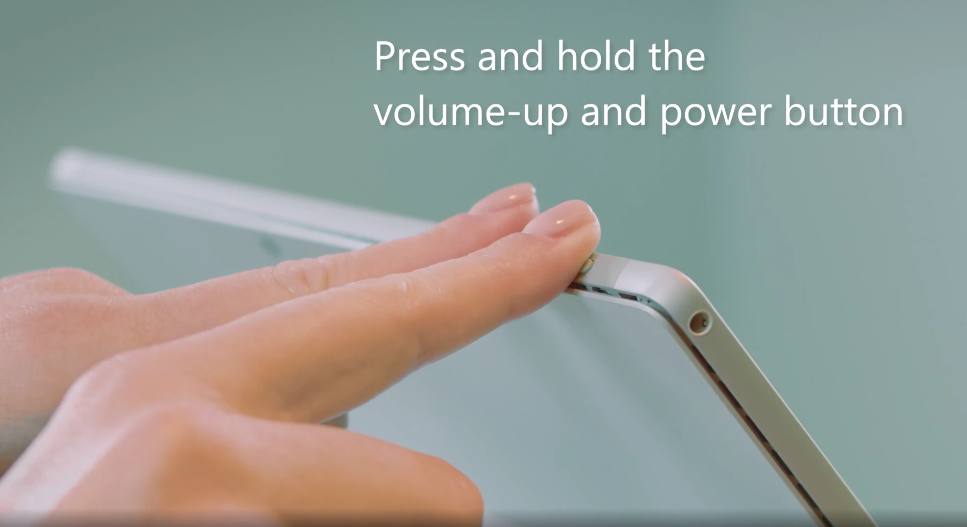 How To Fix Microsoft Surface Keyboard That Isn't Working? 3 Close-up of a person pressing and holding the volume-up and power buttons on an older Microsoft Surface Pro to perform a restart.